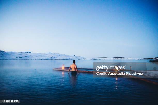 man met bad in thermaal zwembad met uitzicht op de besneeuwde bergen en bevroren meer in ijsland - winter swimming pool stockfoto's en -beelden