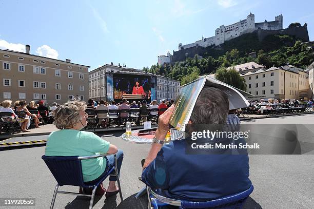 People watch the live broadcast of the opening reception on a screen at Kapitelplatz during the Salzburg Festival at Felsenreitschule on July 27,...