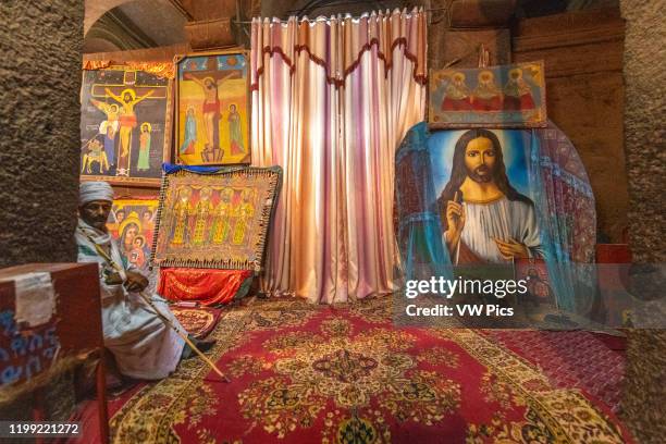 Man sits near a collection of Christian artwork within the church of Bet Medhane Alem in Lalibela , Ethiopia.