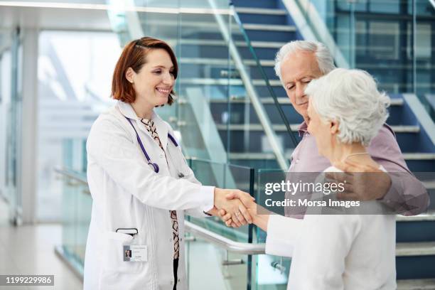 senior-paar zu besuch ärztin im krankenhaus - couple shaking hands with doctor stock-fotos und bilder