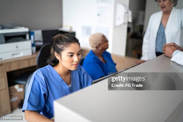 secretaria que trabaja en la recepción del hospital - clinica medica fotografías e imágenes de stock