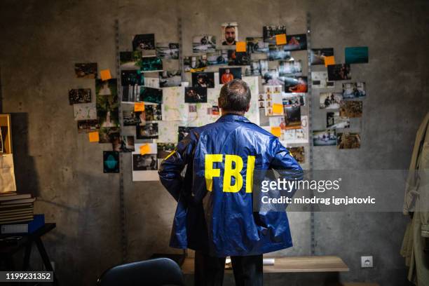 fbi detective looking at wall full of evidences and crime scene pictures - fbi stock pictures, royalty-free photos & images