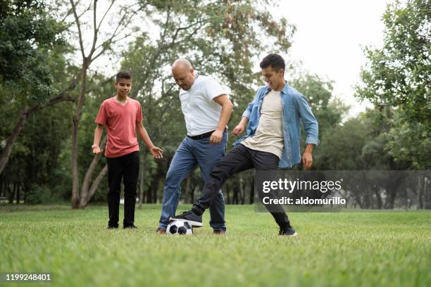 fun latin father and teenage sons playing with soccer ball - handsome teen boy outdoors stock pictures, royalty-free photos & images