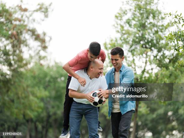 spaß latin vater spielen mit söhnen draußen mit fußball - latin father and son stock-fotos und bilder