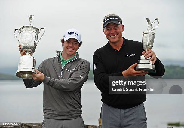 Rory McIlroy and Darren Clarke of Northern Ireland hold the US OPen and British Open Trophies as the pose for a photograph by the lake during the pro...