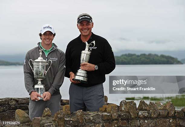 Rory McIlroy and Darren Clarke of Northern Ireland hold the US OPen and British Open Trophies as the pose for a photograph by the lake during the pro...