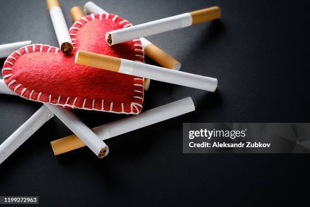 cigarettes lie on a red decorative heart, on a black background. smoking destroys health. social problem. - smoke heart stock-fotos und bilder