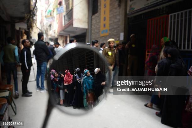 Voters are seen reflected on a mirror as they queue at a polling station to cast their votes during the Legislative Assembly elections in New Delhi...