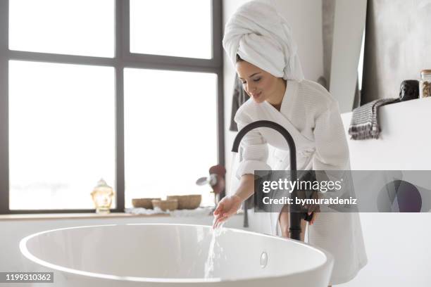 turning on the water of bathtub at home - bathtub stock pictures, royalty-free photos & images