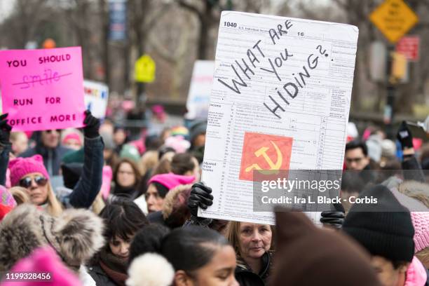 Marcher in a group with a sign that say "What Are You Hiding?" on a sign made from a 1040 Tax Return and the Hammer and Sickle of the Russian...