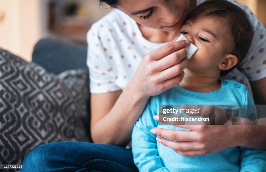 Mother helping her baby son to blow his nose