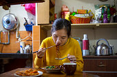 Asian woman eating noddle using chopsticks at home