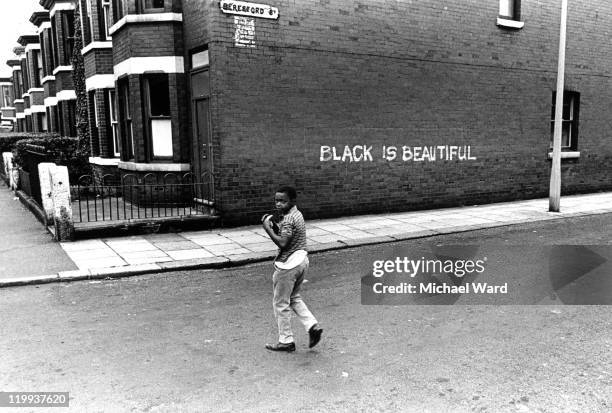 Boy looks over his shoulder on Beresford Street in Rusholme, Manchester, where 'Black is Beautiful' is written on a wall, 1969.