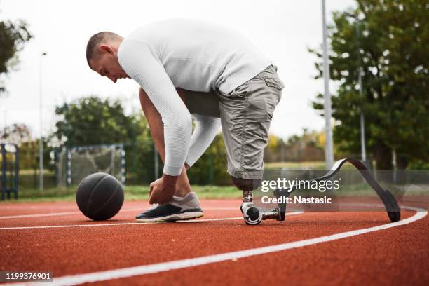 giovane uomo con arto artificiale su un campo da basket legando lacci delle scarpe - piede artificiale per lo sport foto e immagini stock