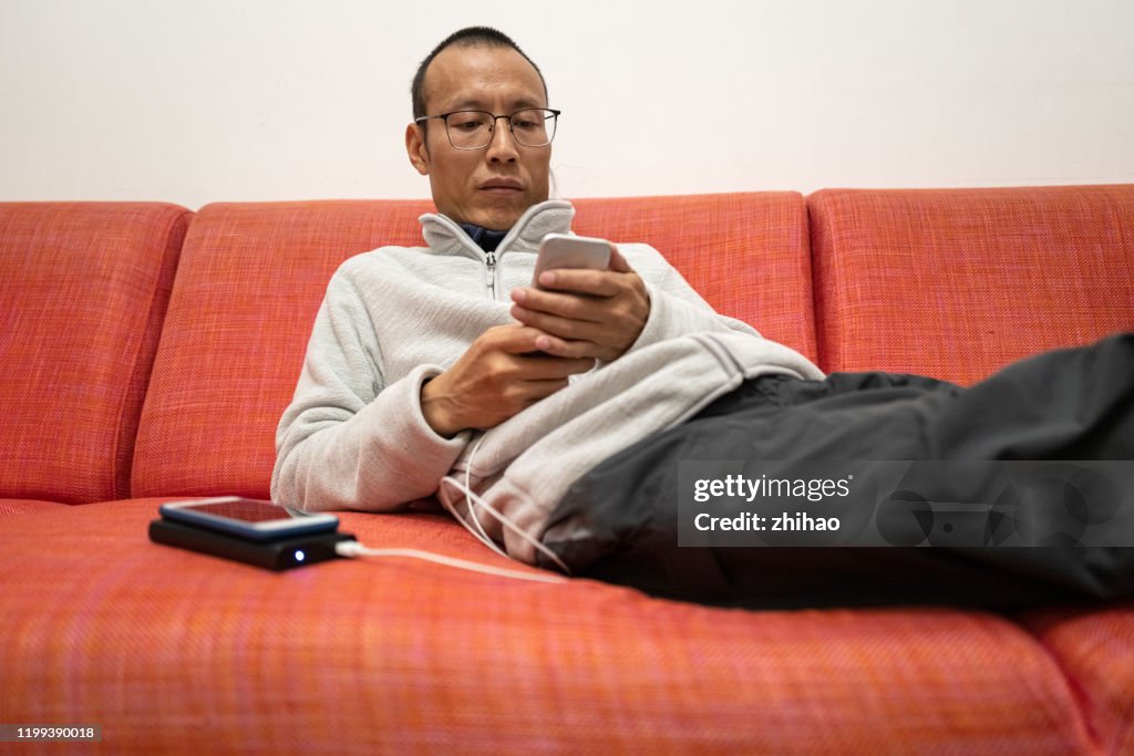 Asian man using charging smartphone on sofa