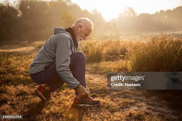 senior man tying shoelaces on sports sneakers - senior athlete stock pictures, royalty-free photos & images