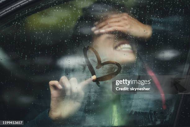 happy woman drawing heart on car window during rainy day. - touching car stock pictures, royalty-free photos & images