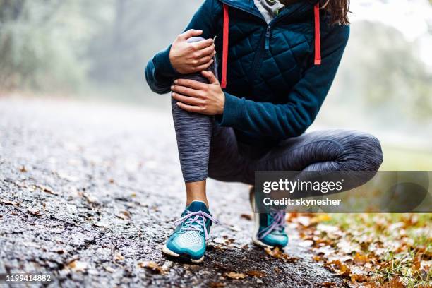 unrecognizable athlete holding her knee in pain at the park. - women sport injury imagens e fotografias de stock