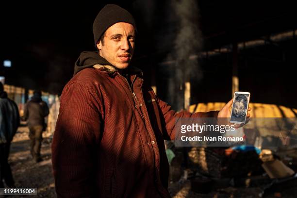 Algerian migrant named Salim inside an abandoned industrial warehouse, shows the cell phone broken by the Croatian border police while trying to...