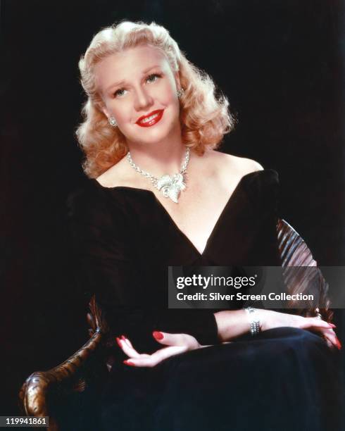 Ginger Rogers , US actress and dancer, wearing a low-cut V-neck outfit, with an ornate silver necklace, in a studio portrait, against a black...