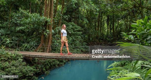 young woman wandering in tropical rainforest walking on bridge over turquoise lagoon - costa rica stock pictures, royalty-free photos & images