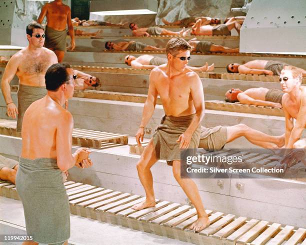 George Peppard , US actor, with a towel wrapped around his waist, and wearing a pair of solarium goggles, as he nervously looks at three approaching...