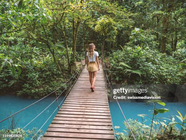 jonge vrouw die in tropisch regenwoud loopt op brug over turquoise lagune - costa rica stockfoto's en -beelden