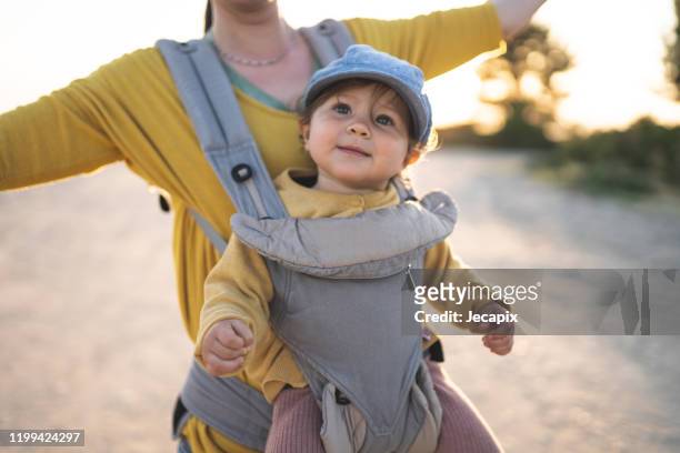 mother walking on the beach with her daughter - baby carrier stock pictures, royalty-free photos & images