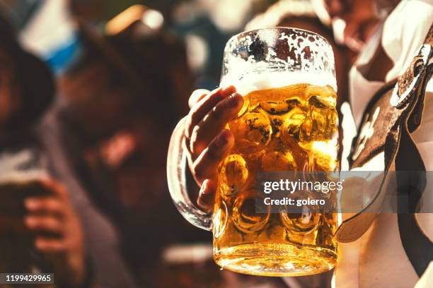 male hand holding mass-beer glass at beer fest in munich - stein stock pictures, royalty-free photos & images