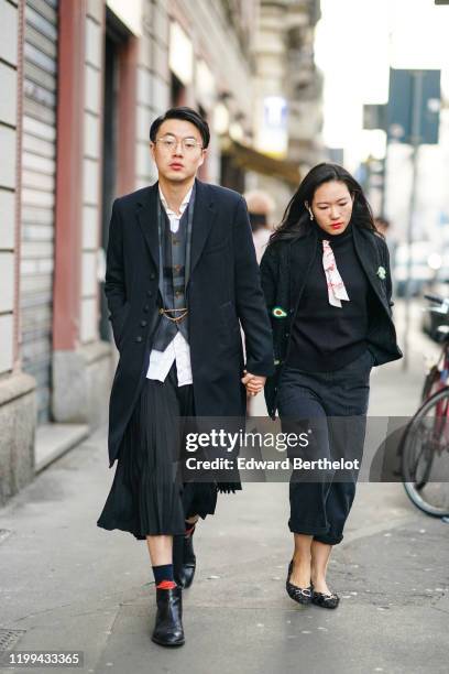 Guest wears glasses, a black long jacket, a white shirt, a checked vest, a black pleated skirt, black leather shoes, socks, outside Reshake, during...