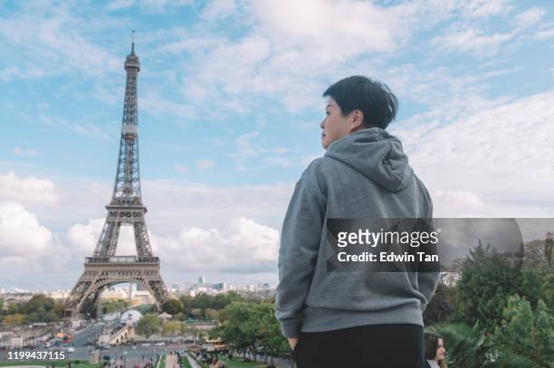 an asian chinese female traveler rear view in front of eiffel tower during day - sassy paris stock pictures, royalty-free photos & images