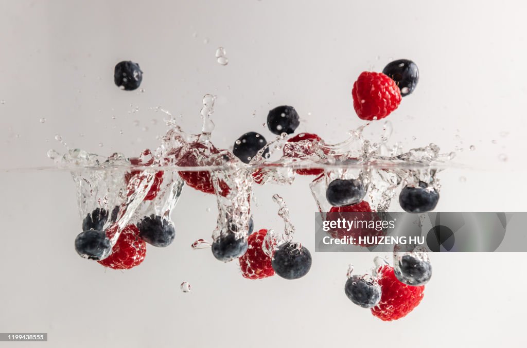 Raspberries and blueberries in water with splash