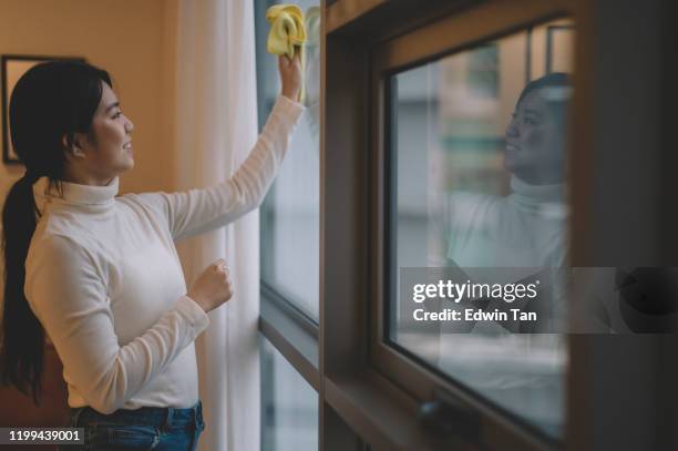 an asian chinese teenage girl cleaning up her living room wiping the window with a yellow cloth - microfiber towel stock pictures, royalty-free photos & images