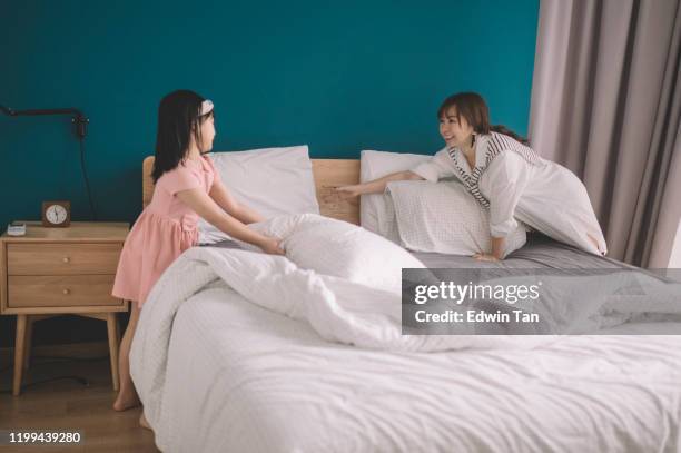 een aziatische chinese moeder maakt het bed samen met haar dochter in de slaapkamer - making bed stockfoto's en -beelden