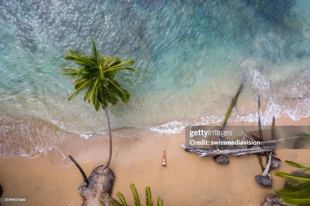 Drohnenansicht der Frau, die sich am goldenen Sandstrand entspannt