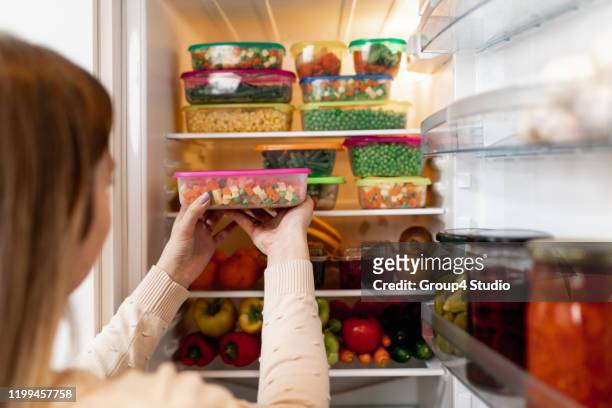 frau nimmt rohkost aus dem kühlschrank - refrigerator stock-fotos und bilder