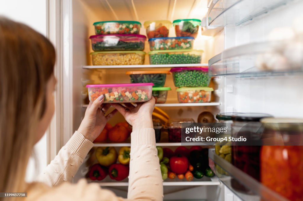 Mujer tomando alimentos crudos del refrigerador