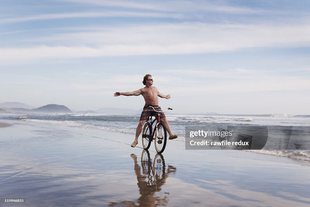 Man riding "no hands" on a bike at the beach