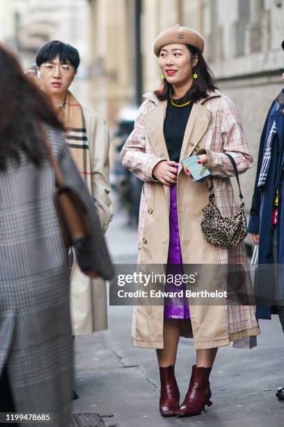 Guest wears a brown beret hat, yellow earrings, a black pullover, a checked trench coat, a purple skirt, burgundy leather boots, outside Reshake,...