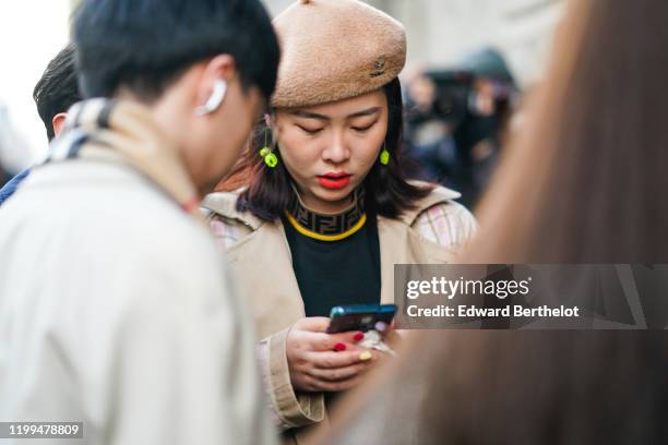 Guest wears a beret hat, neon yellow earrings, a pullover with Fendi collar, a trench coat, outside Reshake, during Milan Fashion Week Menswear...