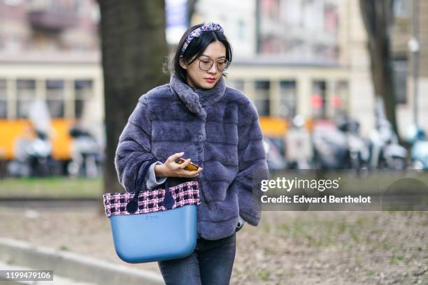 Guest wears a headband, a purple fluffy puffer jacket, a blue "O Bag" with a checked tweed part, outside Reshake, during Milan Fashion Week Menswear...