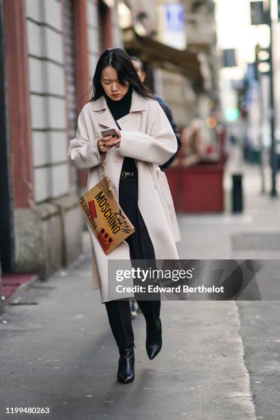 Guest wears a white long coat, black pointy shoes, a turtleneck pullover, a Moschino clutch, outside Reshake, during Milan Fashion Week Menswear...
