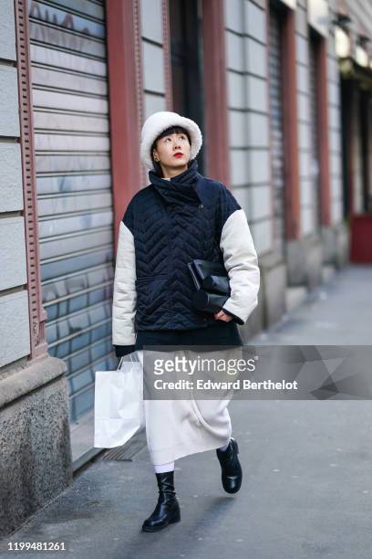 Guest wears a white fluffy hat, a black quilted jacket with white sleeves and turtleneck collar, a white skirt, black leather boots, a leather bag,...