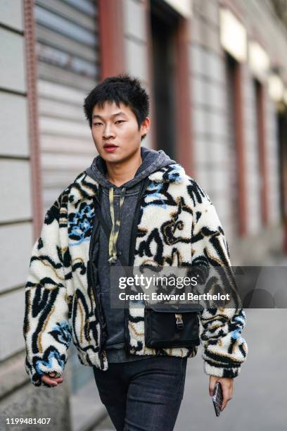 Guest wears a gray hoodie sweater, a black bag, a fluffy winter jacket with geometric printed patterns, black denim jeans, outside Reshake, during...