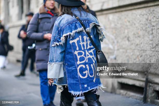 Guest wears a blue denim ripped jacket with printed "The Bad Guy", a black leather studded bag, outside Reshake, during Milan Fashion Week Menswear...