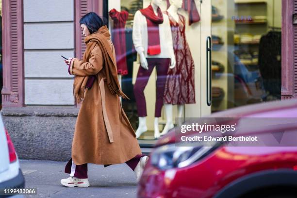 Guest wears a brown scarf, a brown long winter coat, Gucci sneakers shoes, outside Reshake, during Milan Fashion Week Menswear Fall/Winter 2020/2021,...