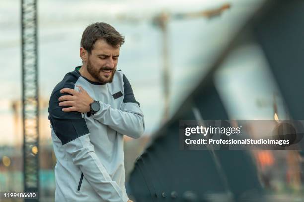 il bel giovane sportivo ha un infortunio fisico alla spalla durante un allenamento - sports pain foto e immagini stock