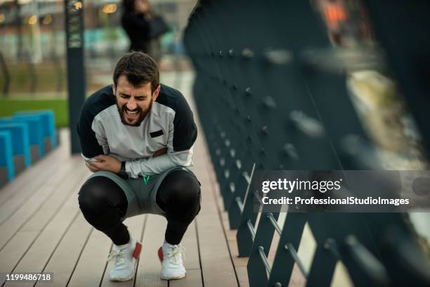 handsome young sportsman haben verletzung des magens während eines trainings - bauchweh stock-fotos und bilder