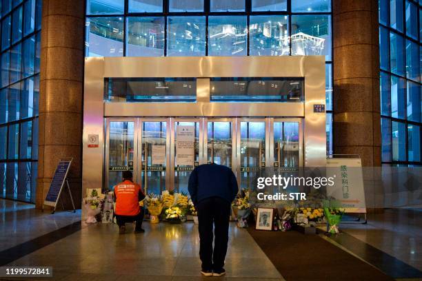 This photo taken on February 7, 2020 shows a man bowing in front of flowers and a photo of the late ophthalmologist Li Wenliang outside the Houhu...