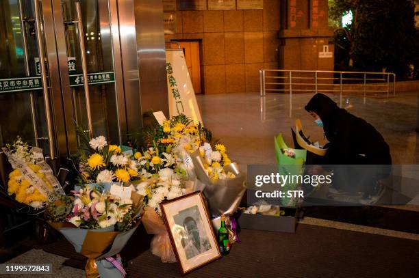 This photo taken on February 7, 2020 shows a man placing flowers beside a photo of the late ophthalmologist Li Wenliang outside the Houhu Branch of...